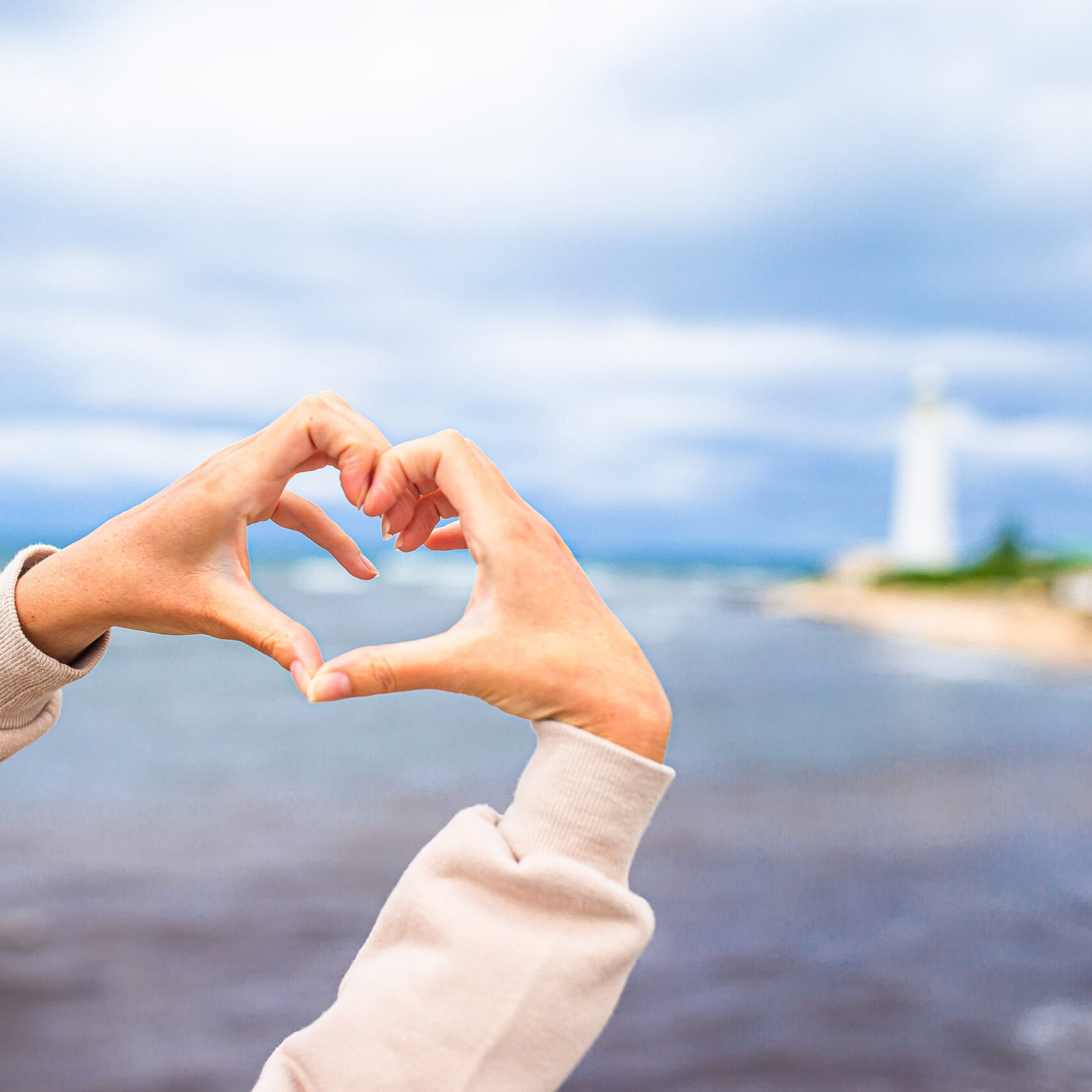 Female hands in the form of heart against the lighthouse Close up of heart made by female hands background the lighthouse